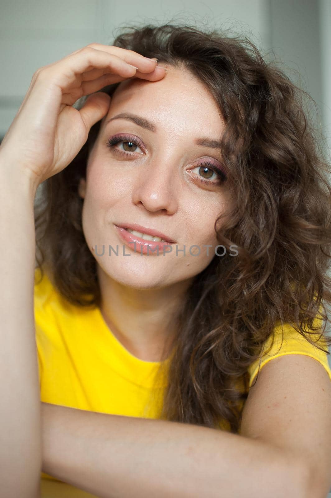 Beautiful curly girl in yellow t-shirt is looking at the camera at home in her apartment, posing with smile, happy people concept by balinska_lv