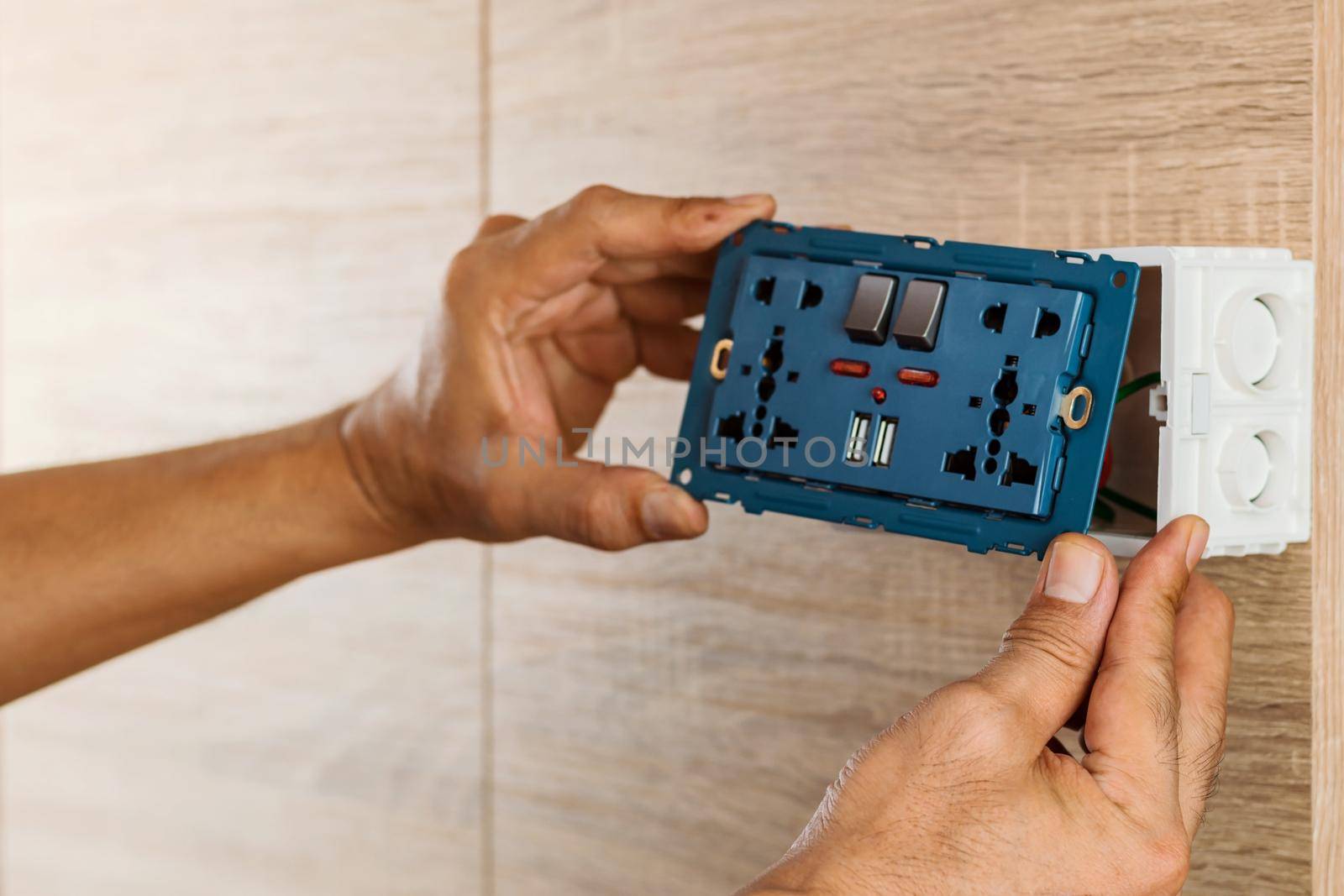 Hand of an electrician are installing the universal wall outlet AC power plug with USB port and on-off in a plastic box on a wooden wall. by wattanaphob