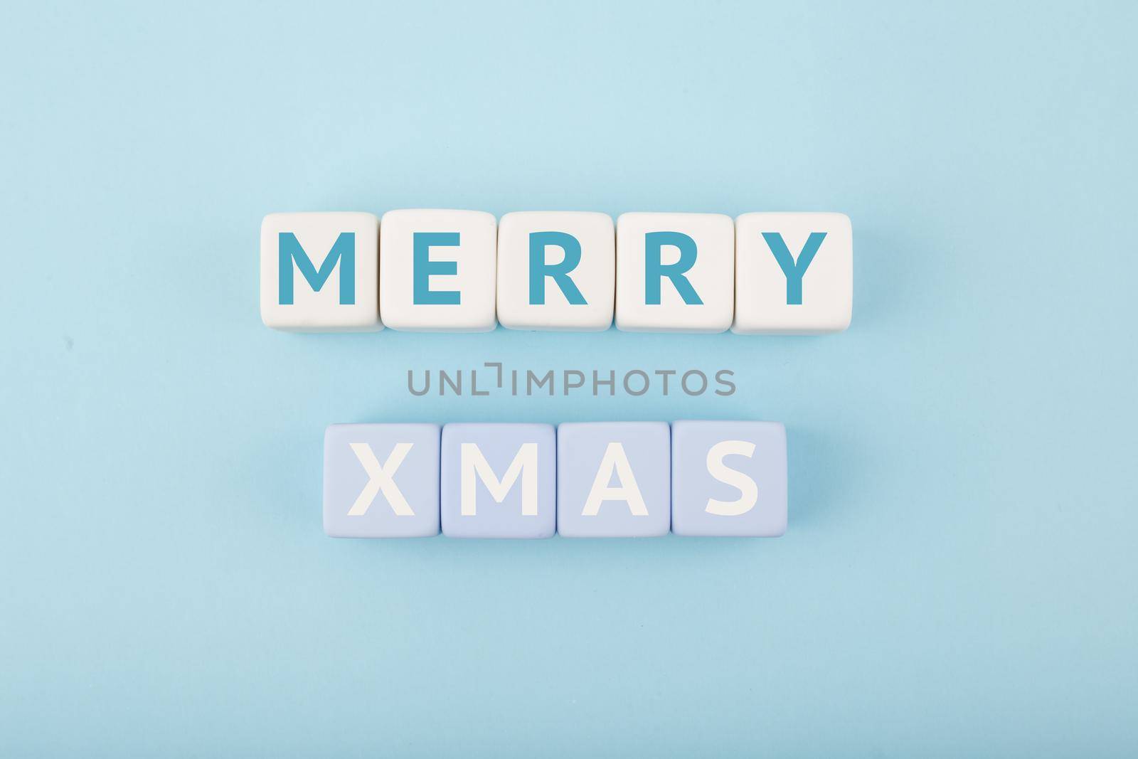 Merry Xmas minimal concept in light pastel blue colors. Handwritten text Merry Christmas on blue tablet against blue background. Modern trendy Merry Xmas concept