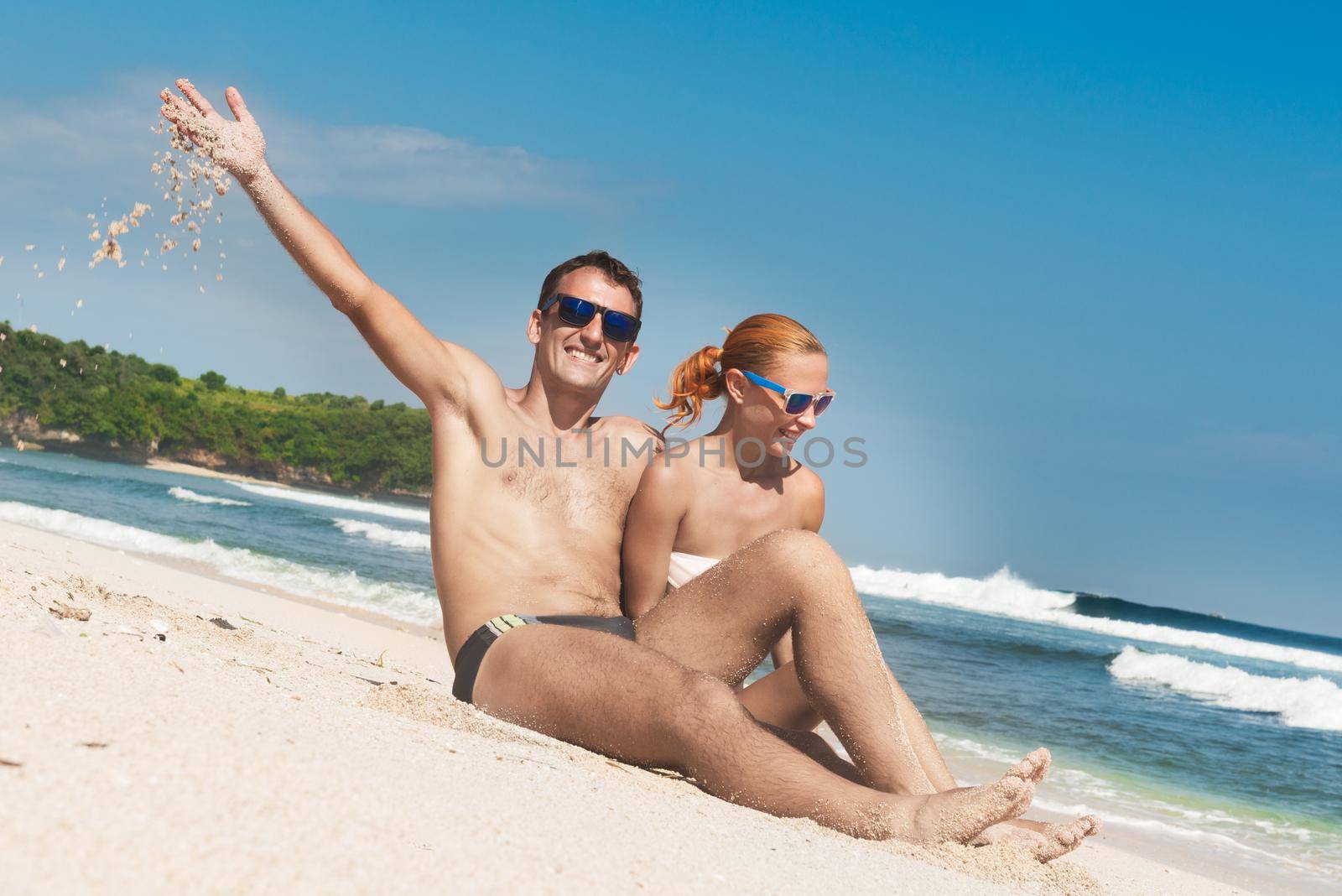 Happy young caucasian couple on sand under sunny summer sun. Travel holidays concept.