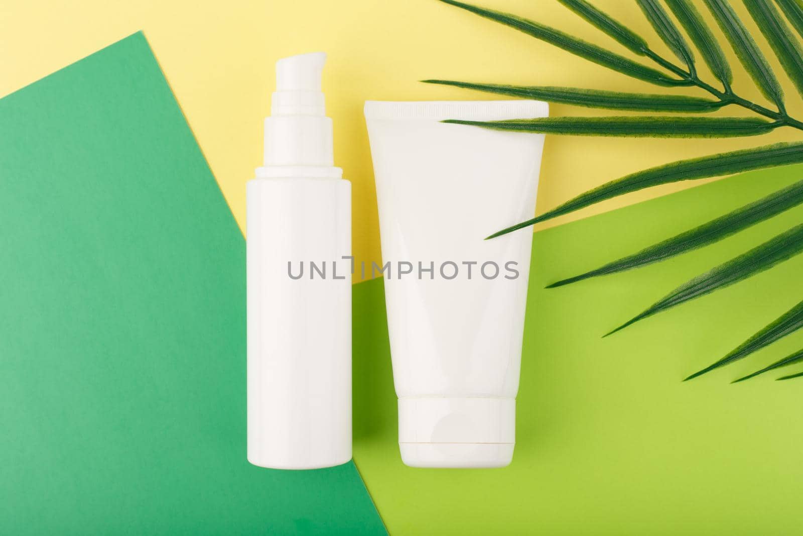Cosmetic products in white unbranded tubes on green and yellow paper with palm leaf by Senorina_Irina