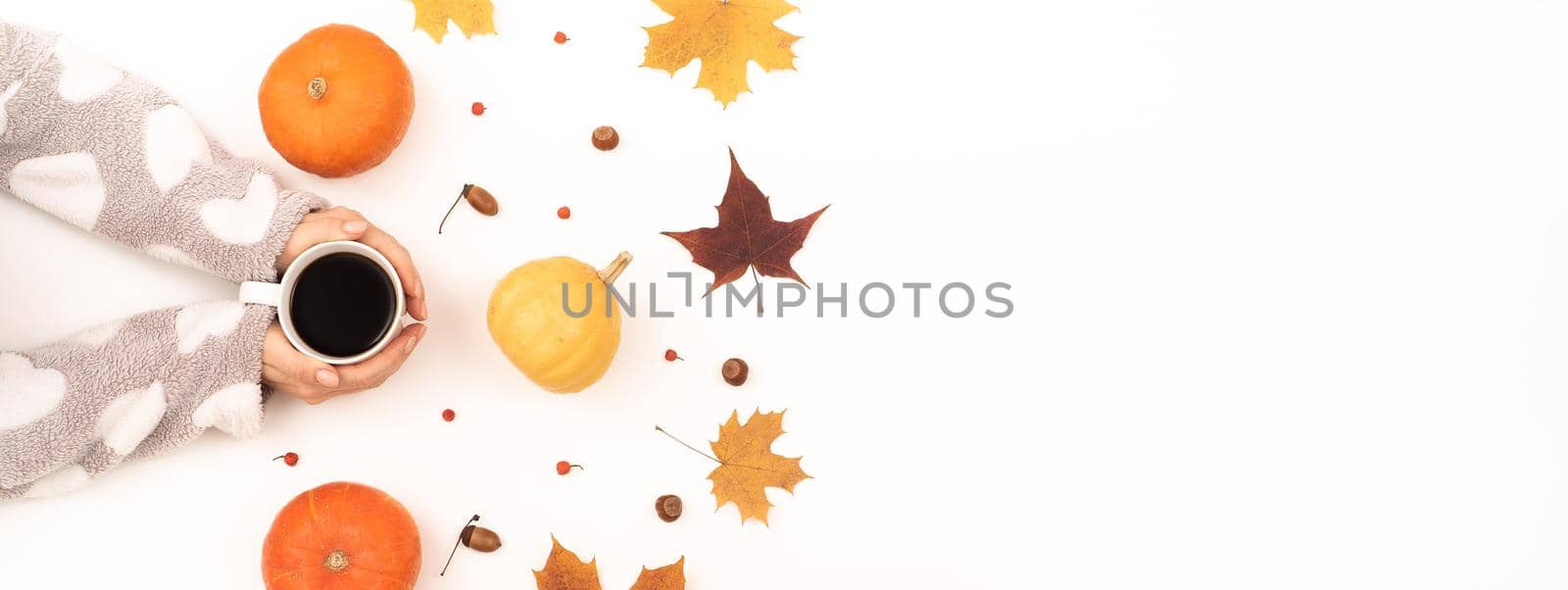 A woman holds a cup of black coffee near the yellow maple leaves of a pumpkin on a white background. Autumn flat lay