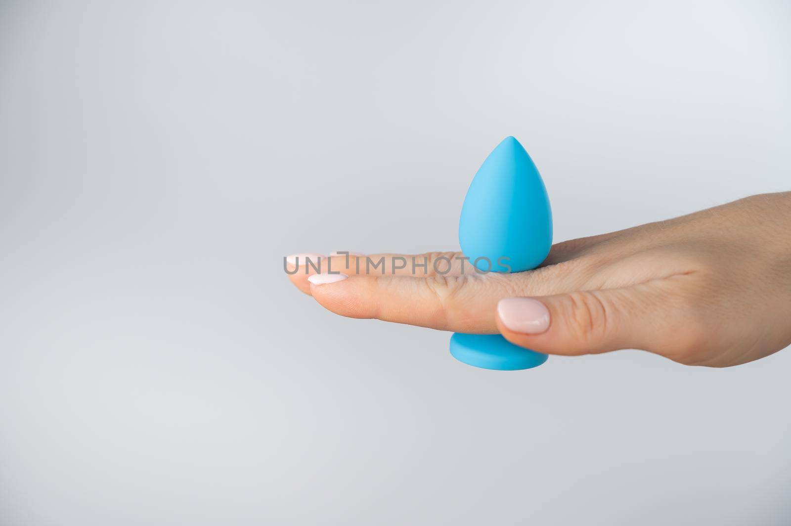 Woman holding a blue butt plug on a white background. Adult toy for alternative sex.