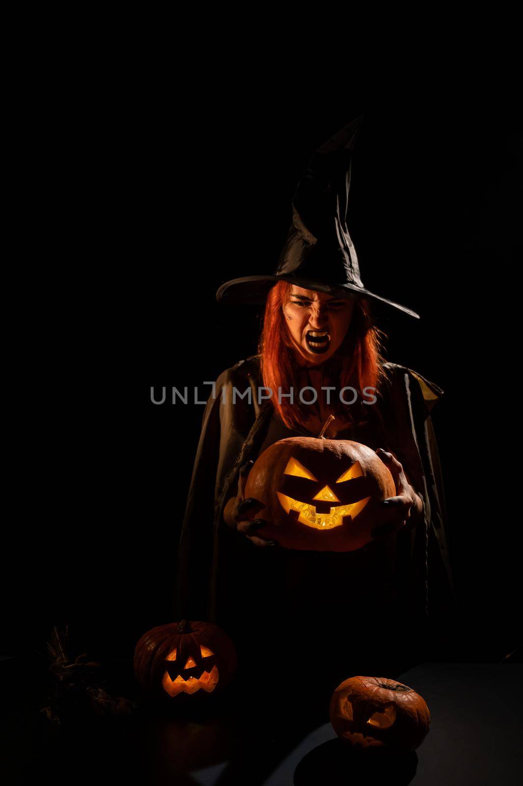 An evil witch holds a halloween jack-o-lantern glowing in the dark by mrwed54