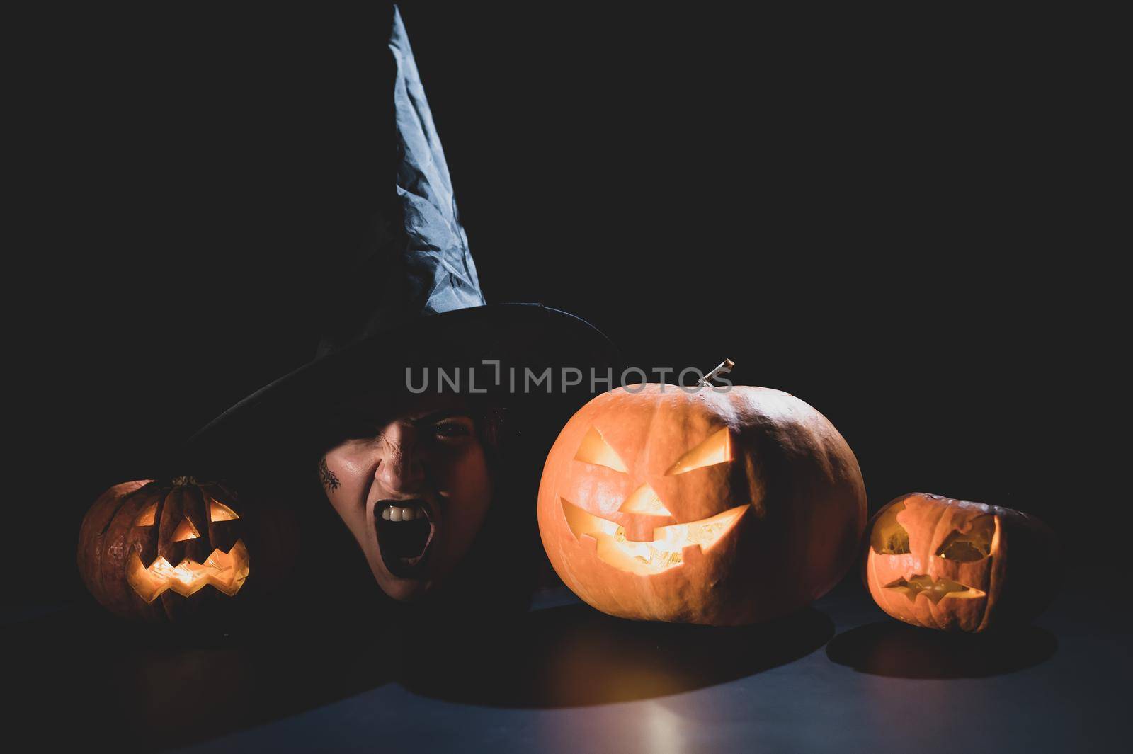 The head of an evil witch is on the table next to the glowing pumpkin jack-o-lantern.