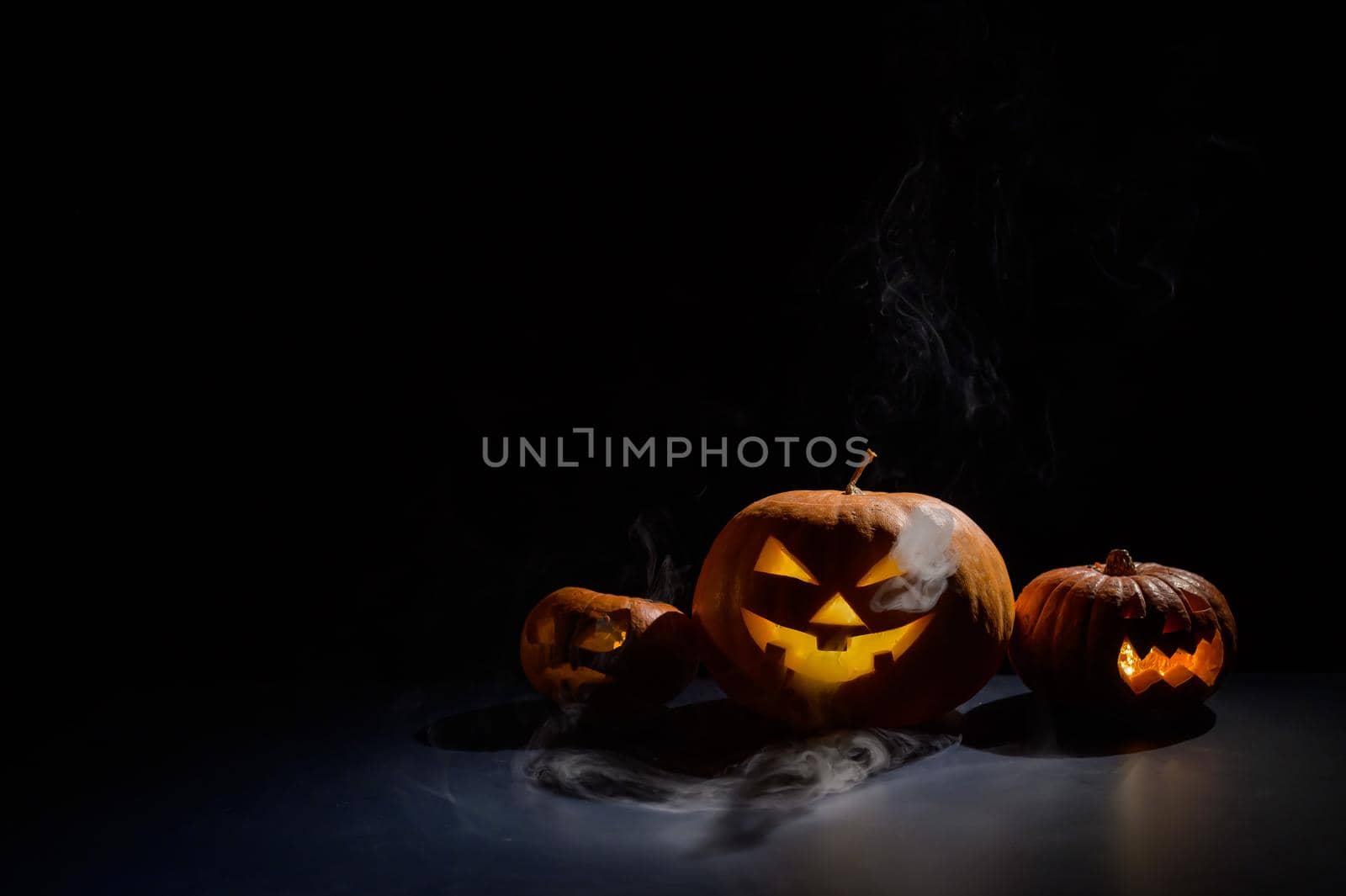 Pumpkins with carved grimaces and candles inside in the dark for halloween. Jack o latern in smoke