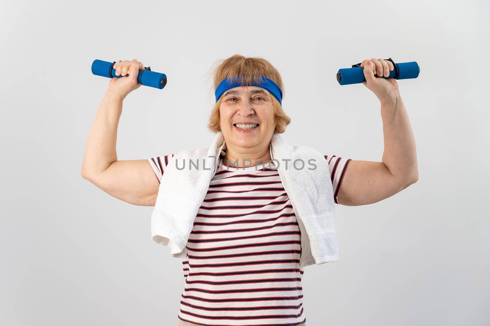 An elderly woman with a blue bandage on her head trains with dumbbells on a white background by mrwed54