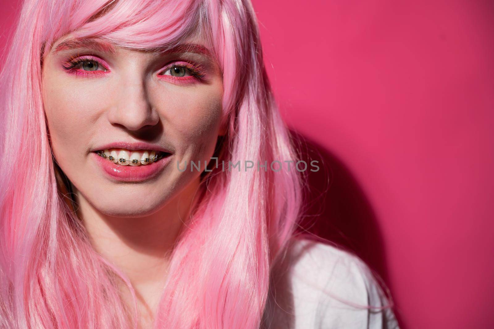 Close-up portrait of a young woman with braces in a pink wig on a pink background