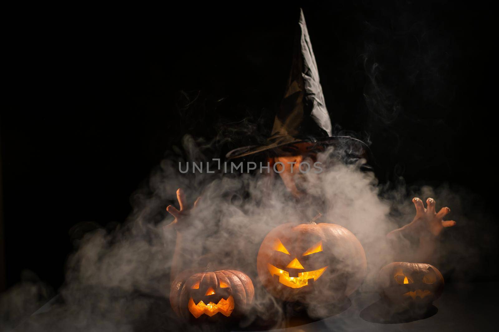 The evil witch casts a spell on pumpkins. Portrait of a woman in a carnival halloween costume in the dark.