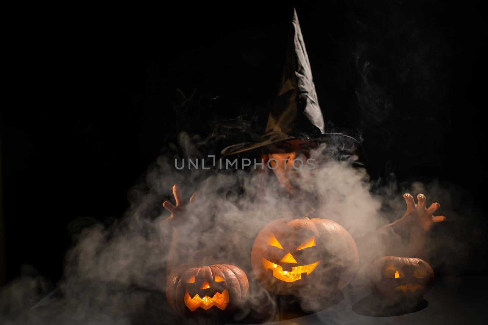 The evil witch casts a spell on pumpkins. Portrait of a woman in a carnival halloween costume in the dark by mrwed54