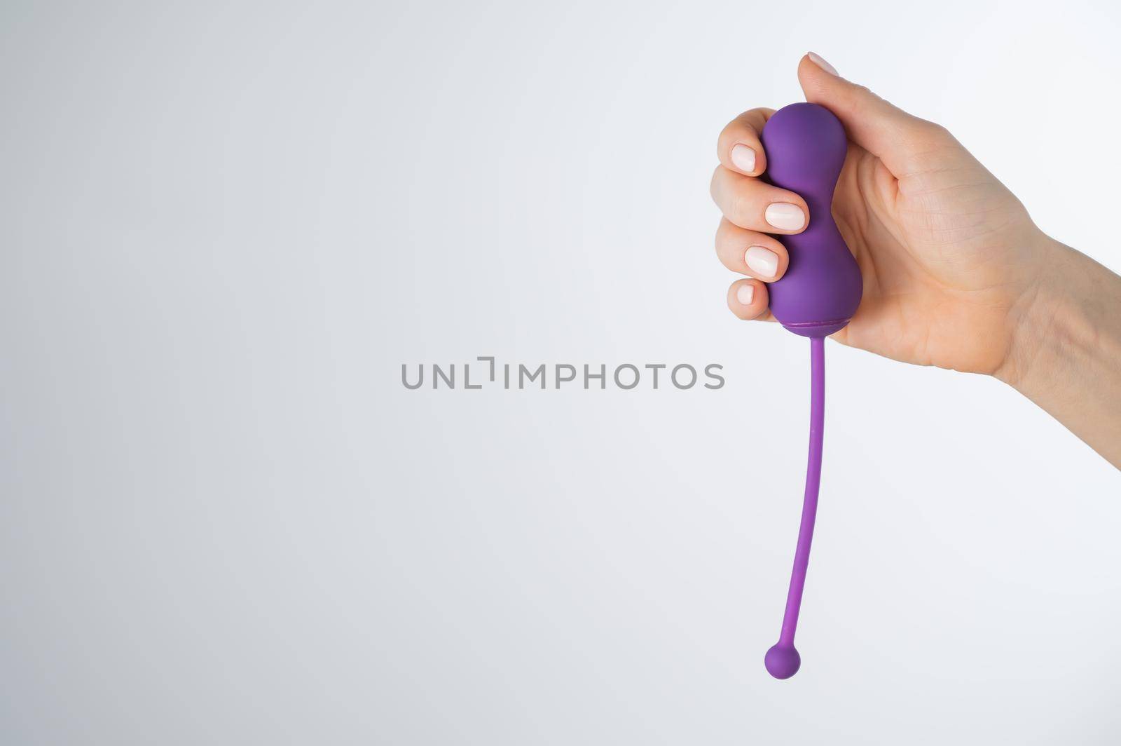 A faceless woman holding an electronic Kegel trainer for training pelvic floor muscles on a white background. Sex toy synchronized with a smartphone.