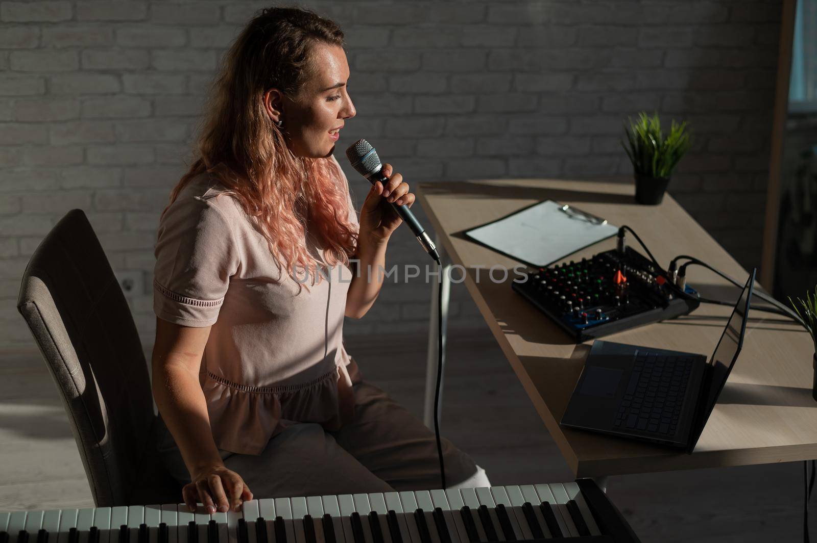 A female blogger sings and plays the live electronic piano. Portrait of a girl recording a song on a web camera and composing on a synthesizer. Online music lessons. Distance learning in quarantine