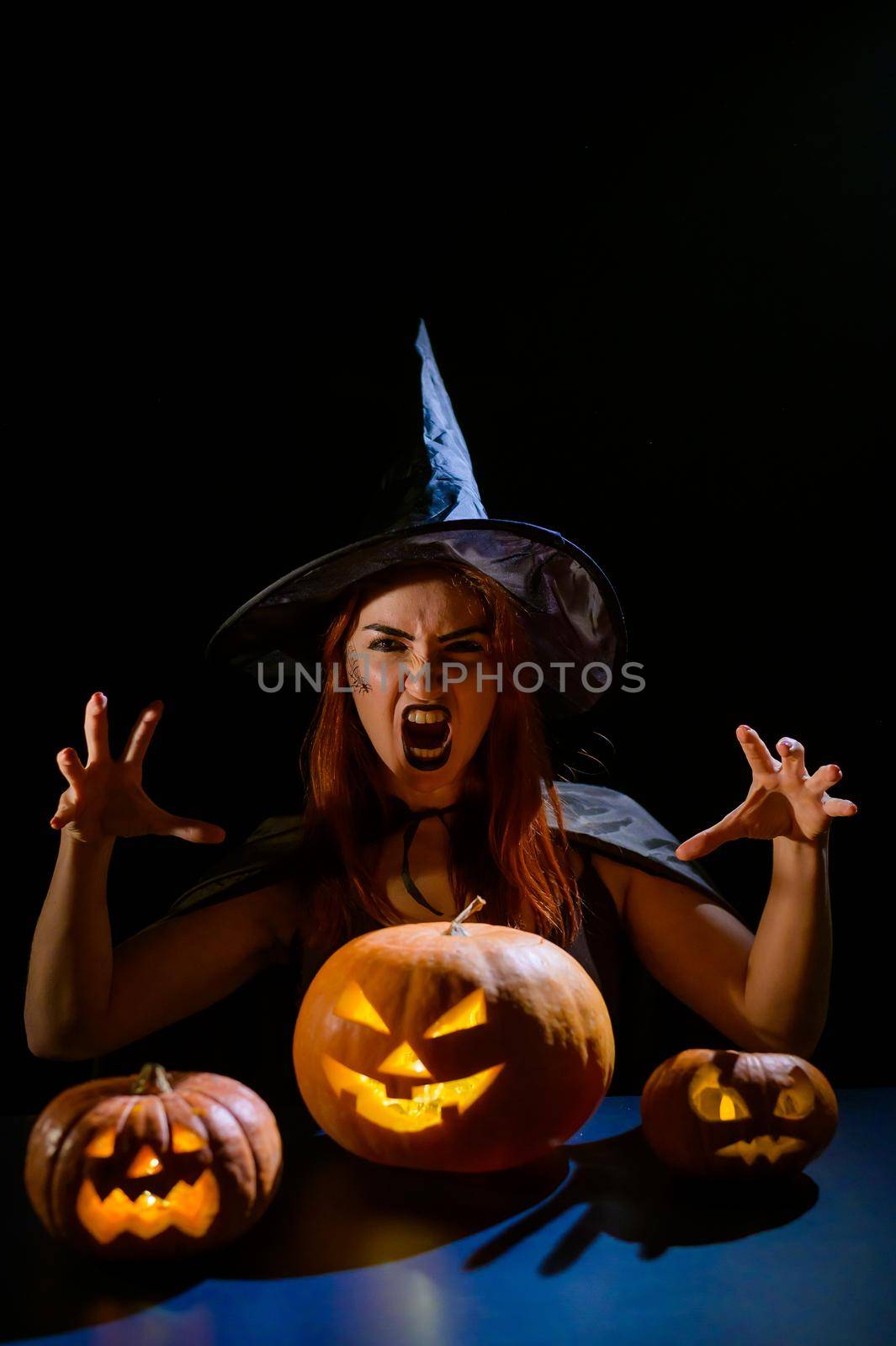 An ominous witch in a hat conjures over a jack-o-lantern. Traditional halloween characters. Mystical fog creeps over pumpkins with carved terrible faces. An evil witch casts a spell. by mrwed54