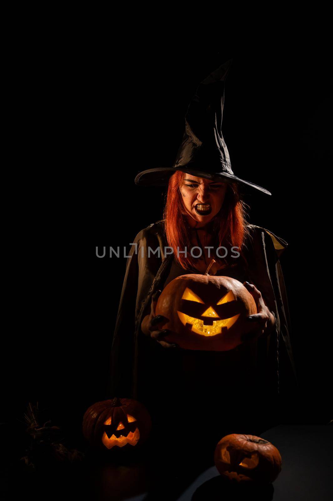 An evil witch holds a halloween jack-o-lantern glowing in the dark by mrwed54