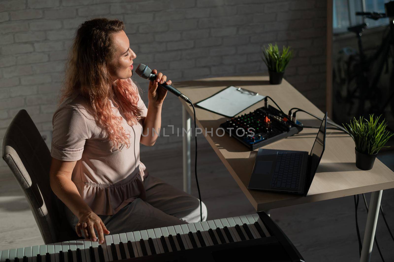 Expressive female singer has a video blog on a laptop. Portrait of a girl recording a song on a web camera and composing on a synthesizer. Online music lessons. Distance learning in quarantine