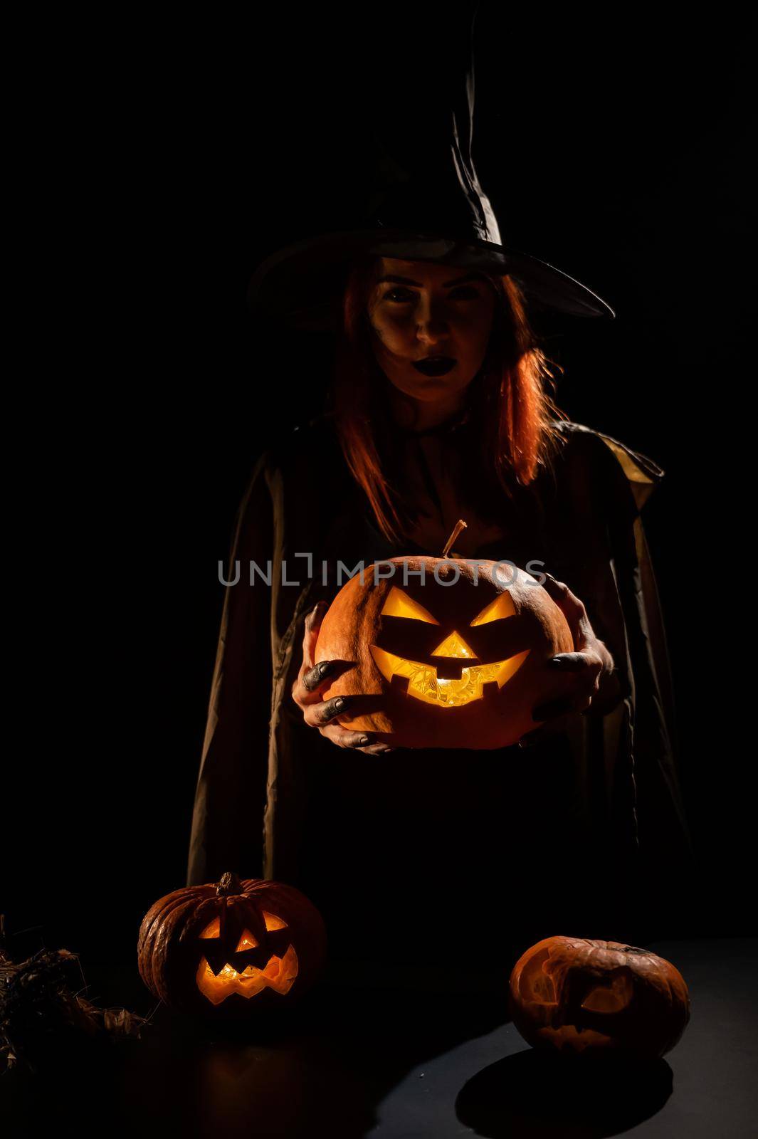 The evil witch casts a spell on pumpkins. Portrait of a woman in a carnival halloween costume in the dark by mrwed54