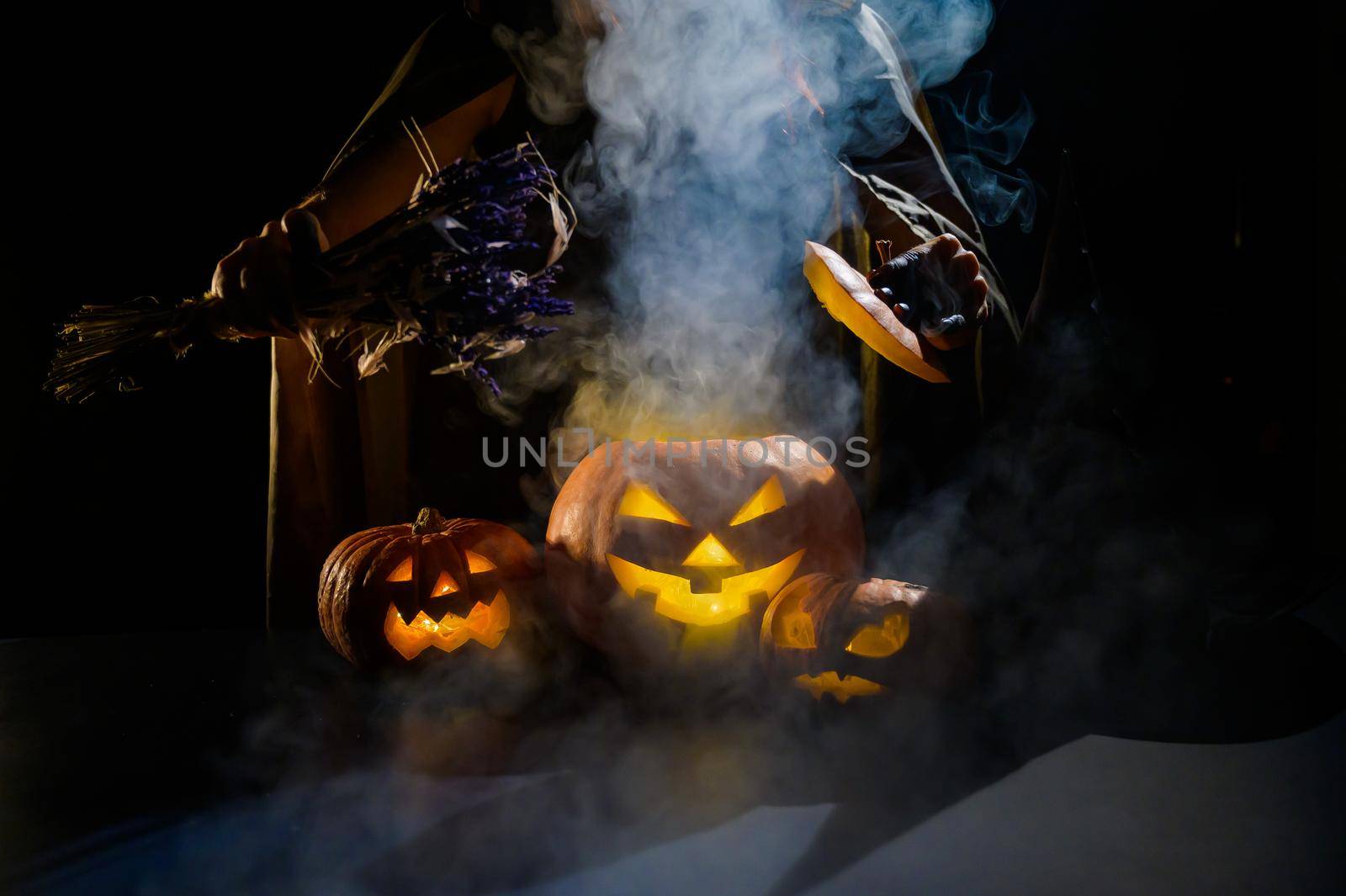 Witch casts a spell on a steaming pumpkin in the dark on Halloween.