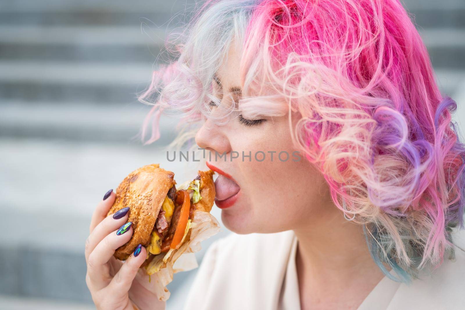 Caucasian woman with curly colored hair eating burger. Bad eating habits and love of fast food by mrwed54