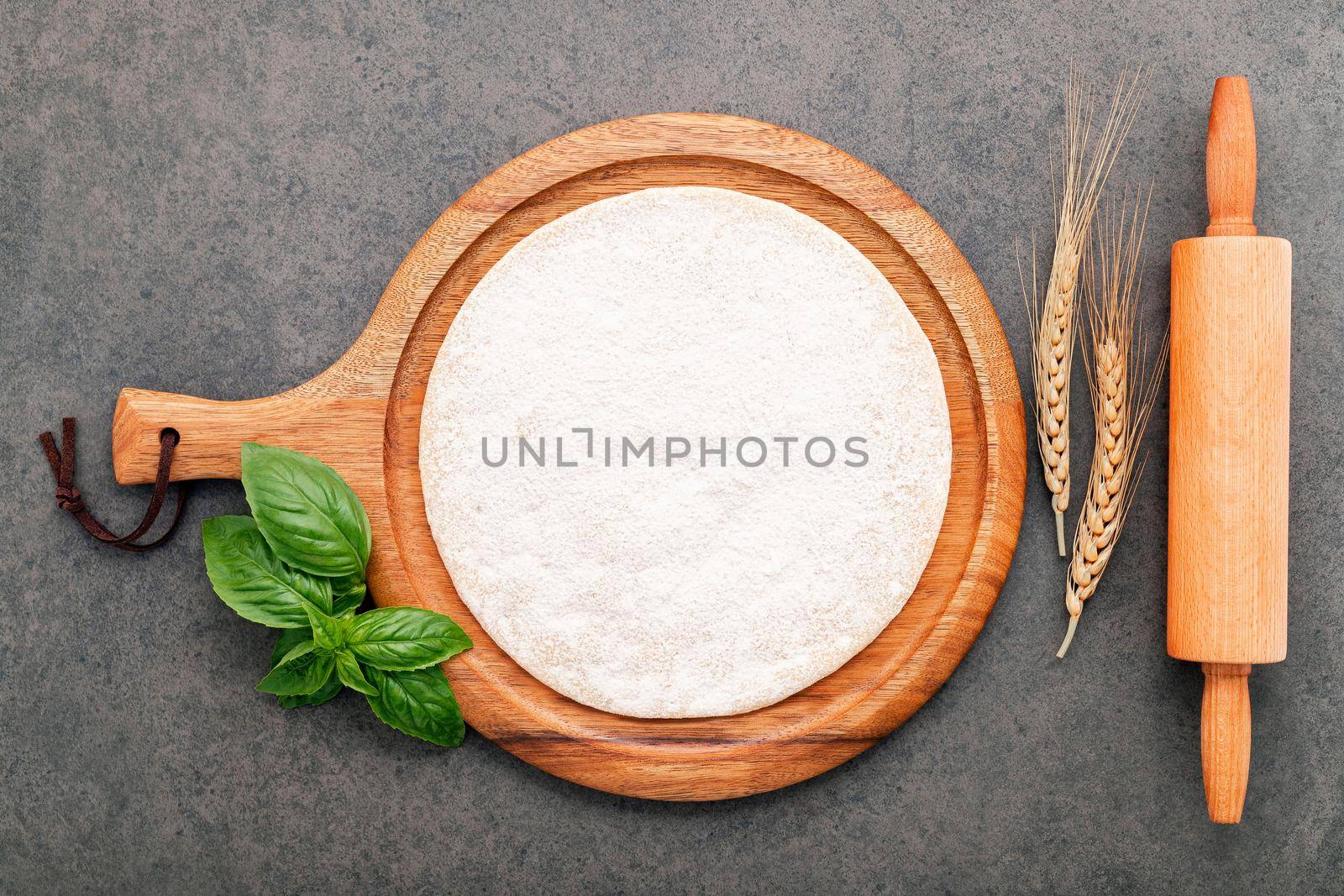 Thin homemade pizza dough with wheat ears  and rolling pin set up on dark concrete background.