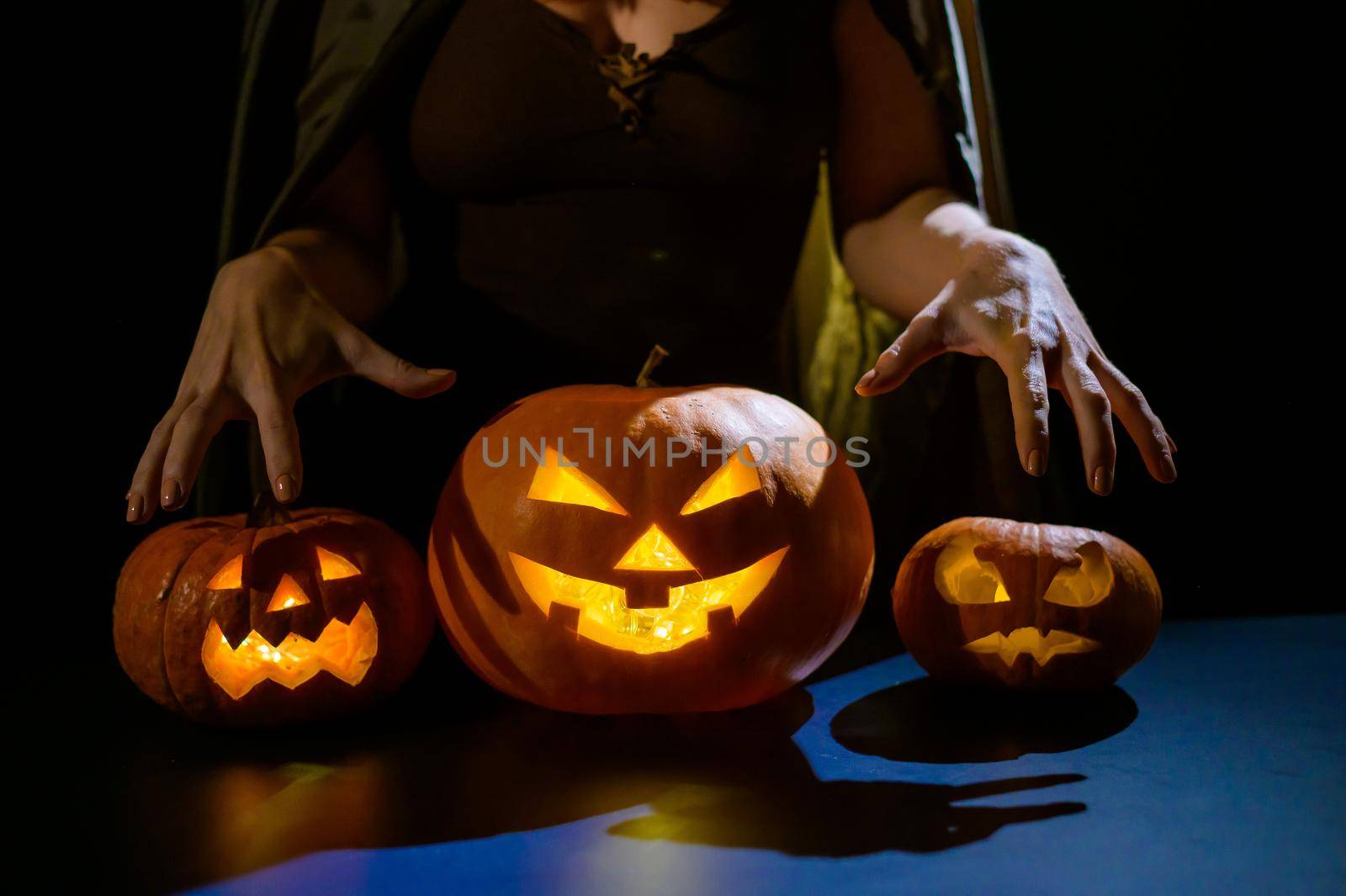 Close-up of female hands on a pumpkin for halloween in a dark studio. The witch is holding a jack-o-lantern by mrwed54