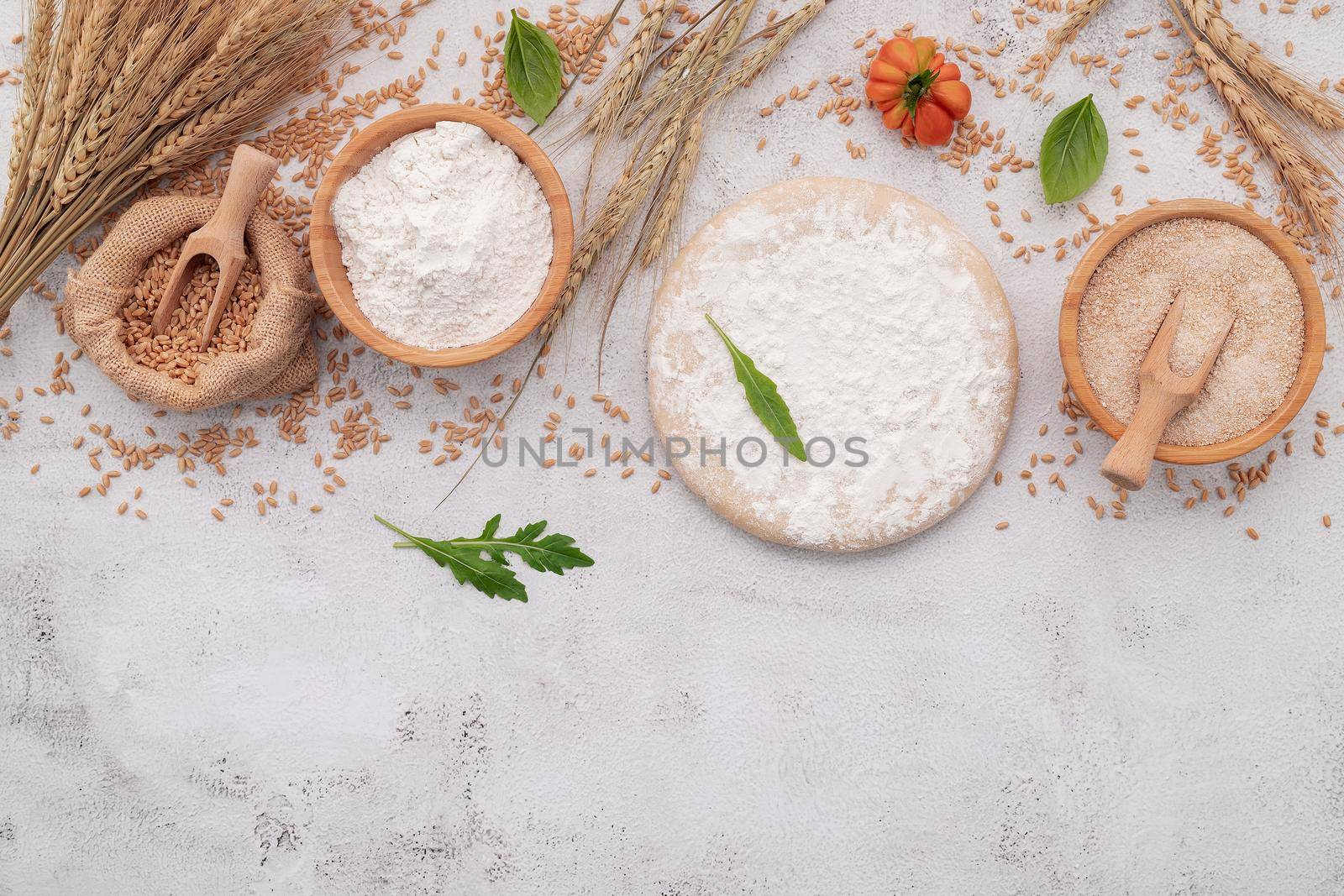 The ingredients for homemade pizza dough with wheat ears ,wheat flour and wheat grains set up on white concrete background.