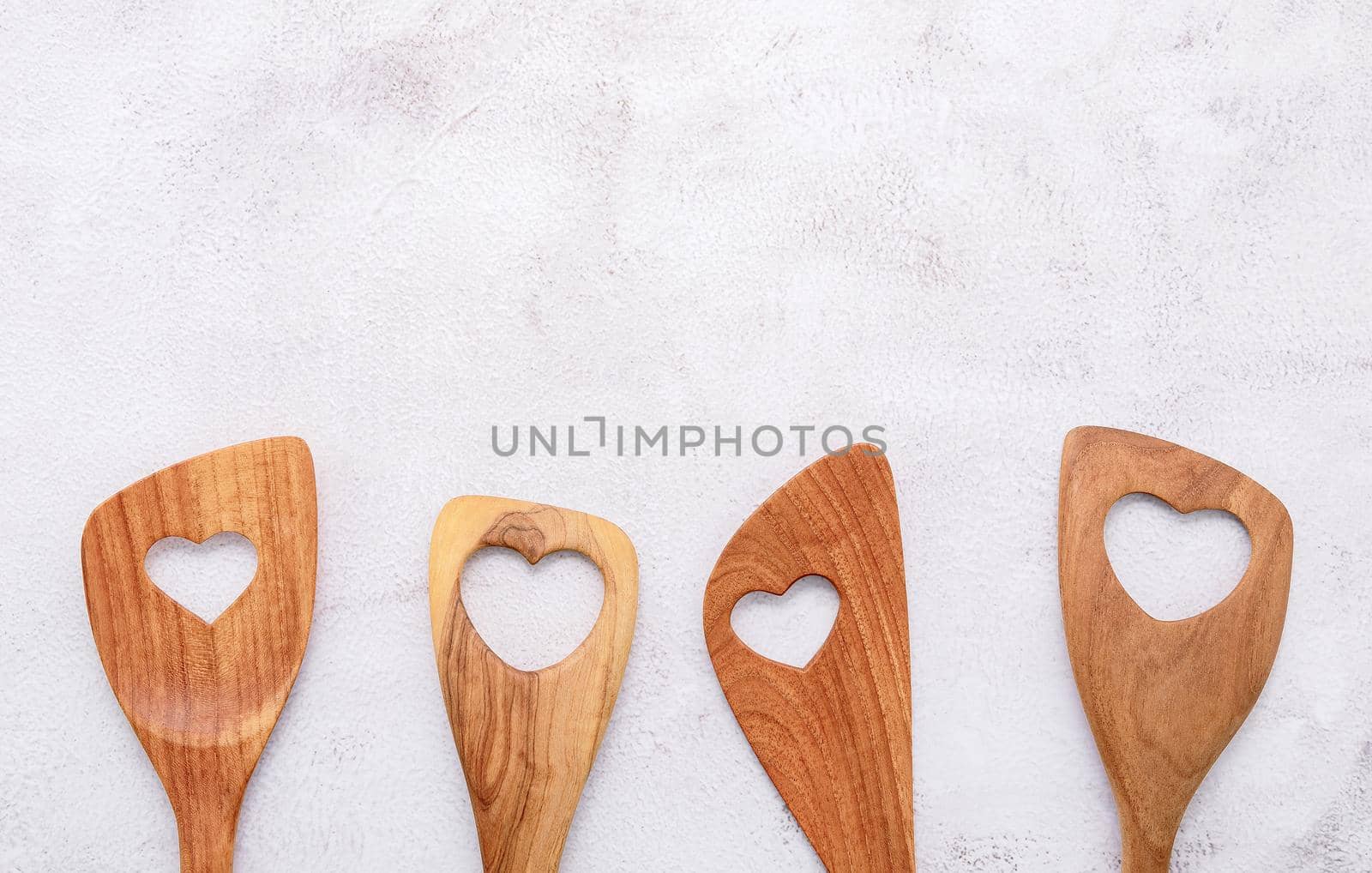 Various heart shape of wooden cooking utensils. Wooden spoons and wooden spatula on white concrete background with flat lay and copy space.