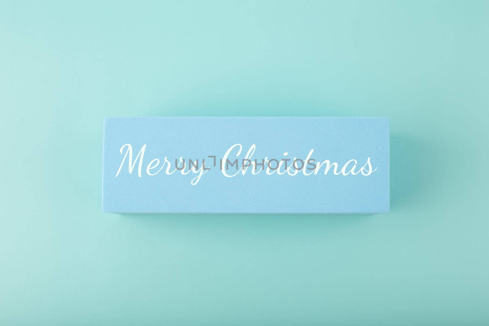Merry Christmas minimal concept in light pastel blue colors. Handwritten text Merry Christmas on blue tablet against blue background. 