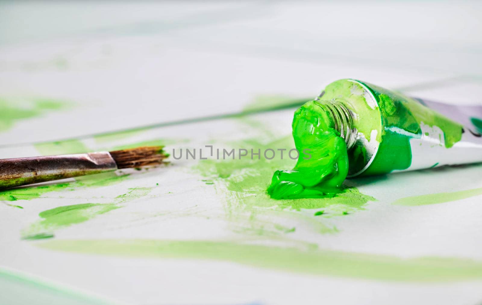 Opend green  watercolor tube  with paint brush on white background with spots of color