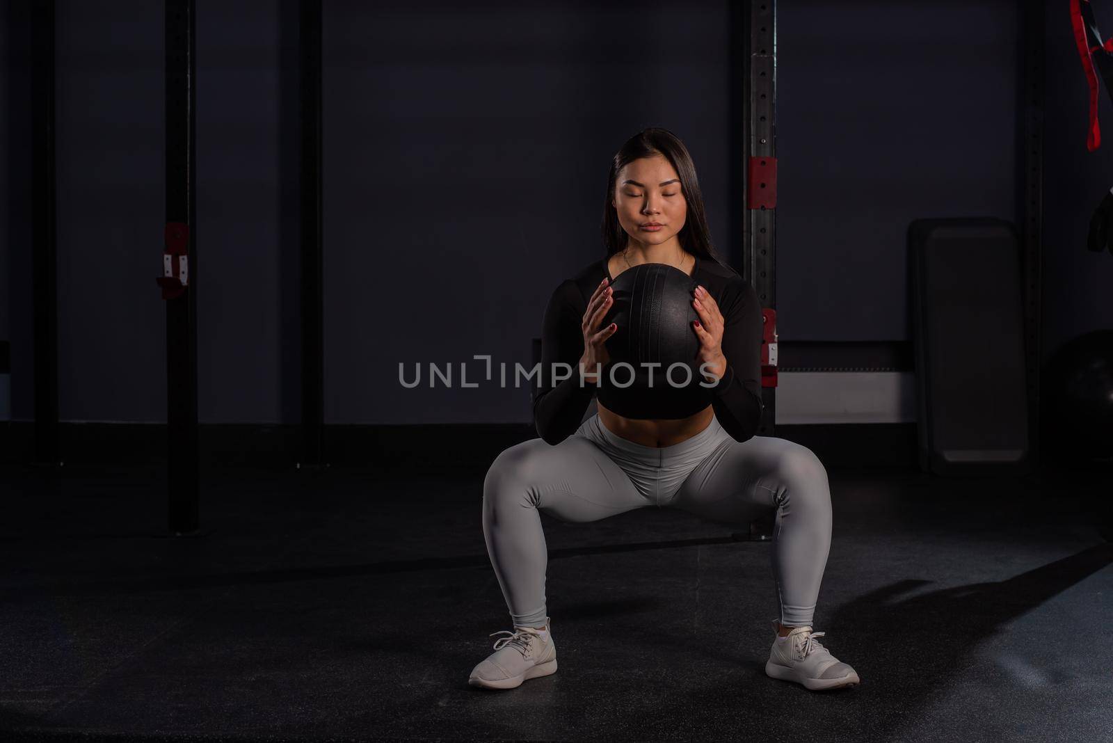 Asian woman squatting with a medicine ball in the gym. by mrwed54