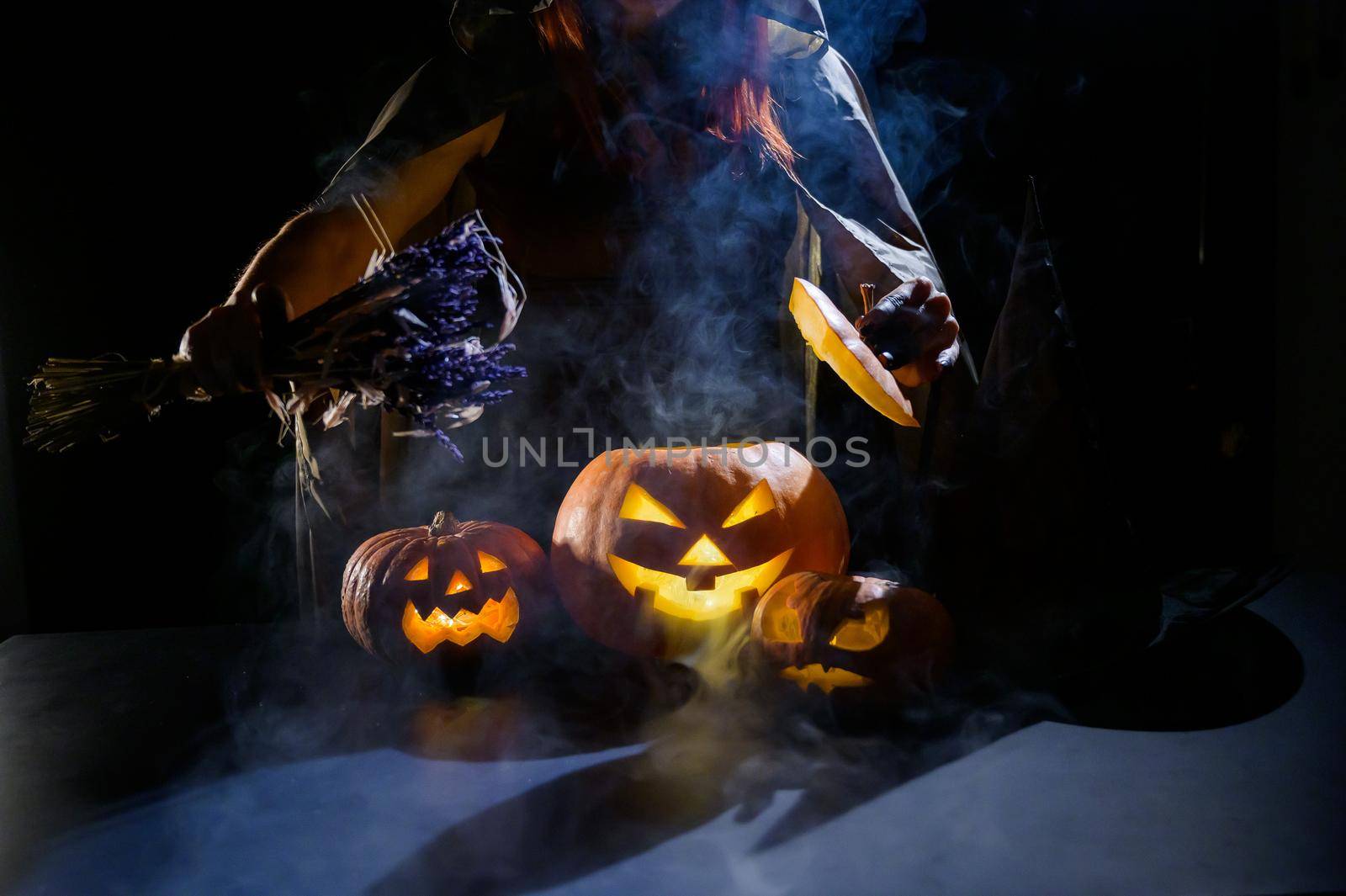 Witch casts a spell on a steaming pumpkin in the dark on Halloween by mrwed54