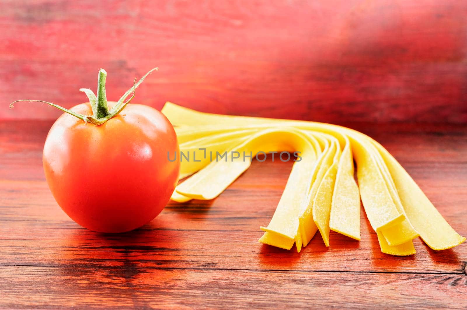 Large flat egg  pasta pappardelle on red wooden background  with  fresh tomato 