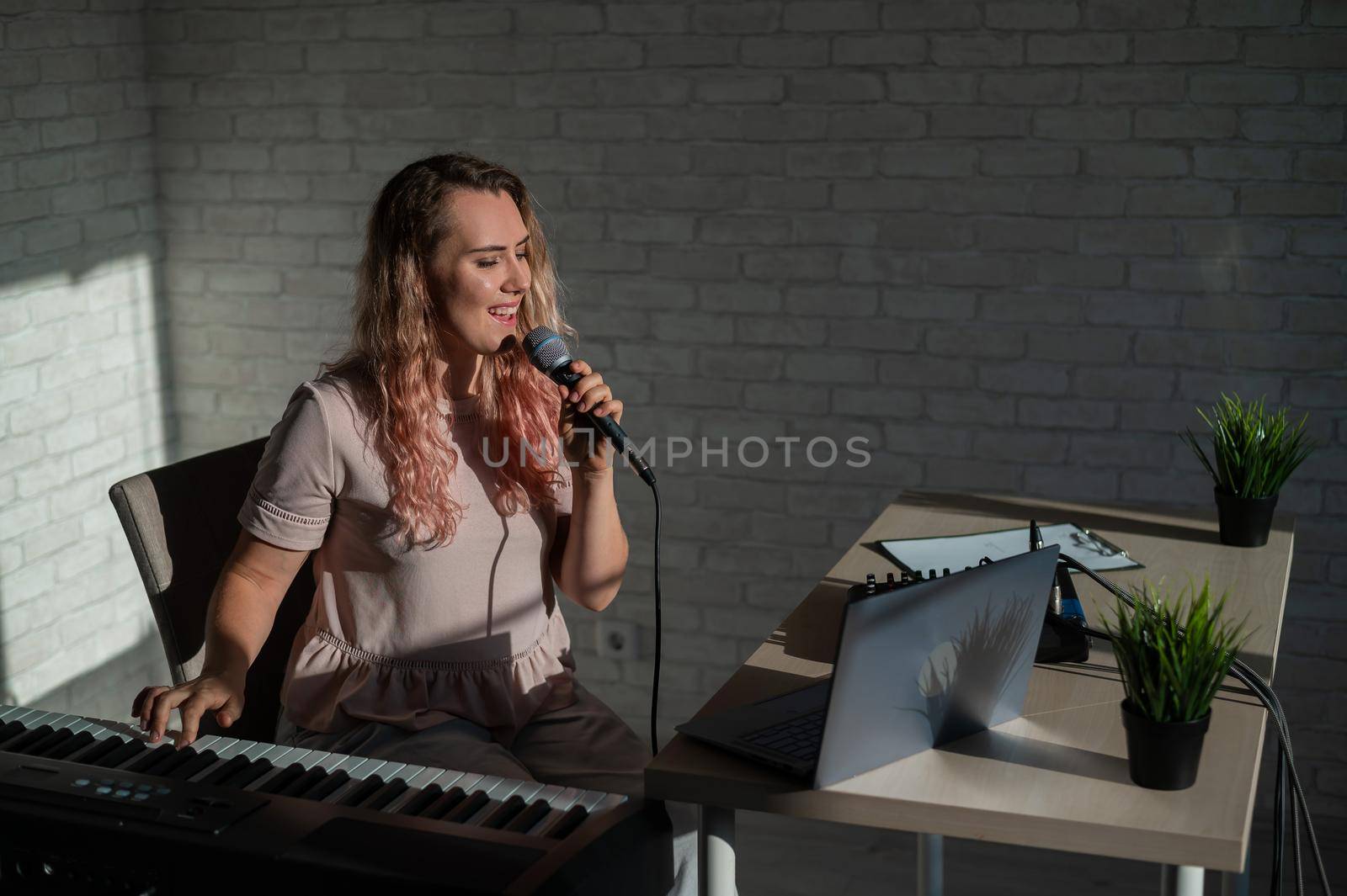 Expressive female singer has a video blog on a laptop. Portrait of a girl recording a song on a web camera and composing on a synthesizer. Online music lessons. Distance learning in quarantine