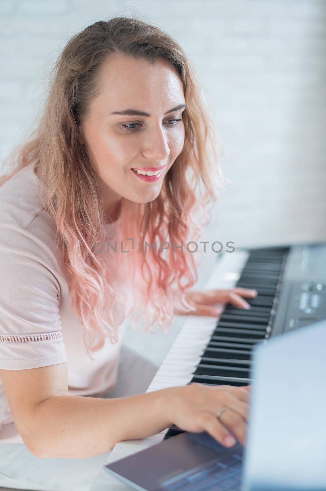 A friendly woman plays the electronic piano and conducts a video blog on her laptop. Stay home. Musical instrument teacher. Distance learning music quarantined