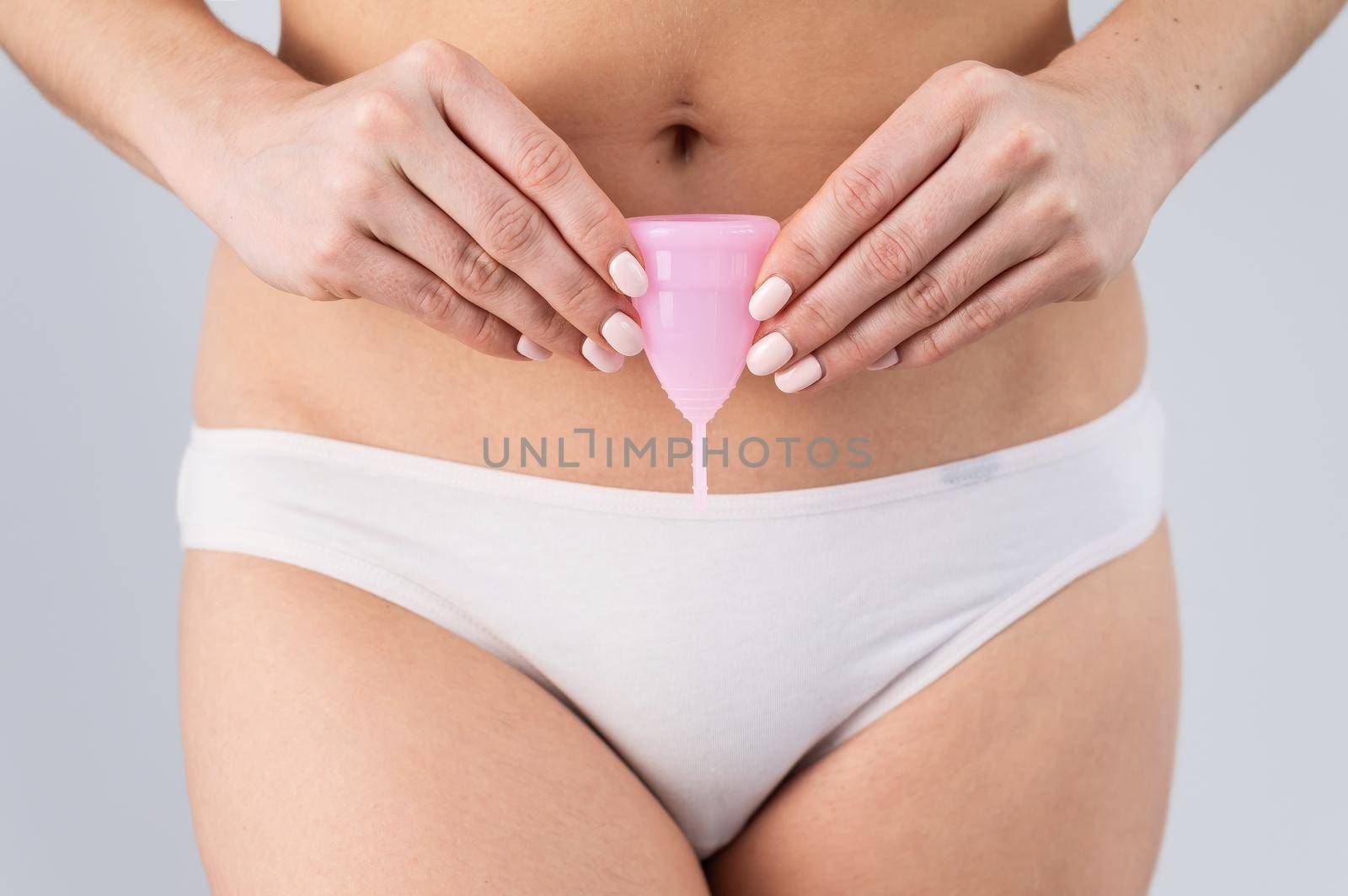 Close-up of a woman in white cotton panties holding a pink menstrual cup against a white background. Alternative to tampons and pads by mrwed54