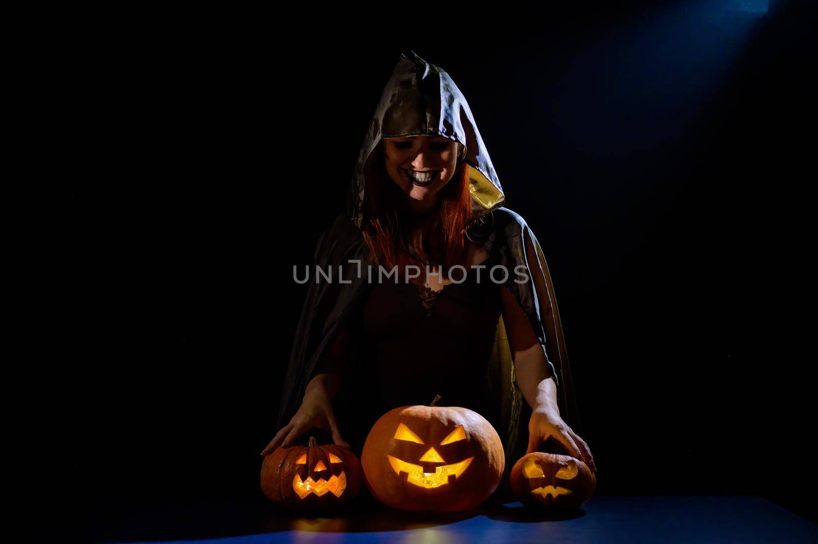 A creepy sorceress in a cloak casts a spell on pumpkins for Halloween.