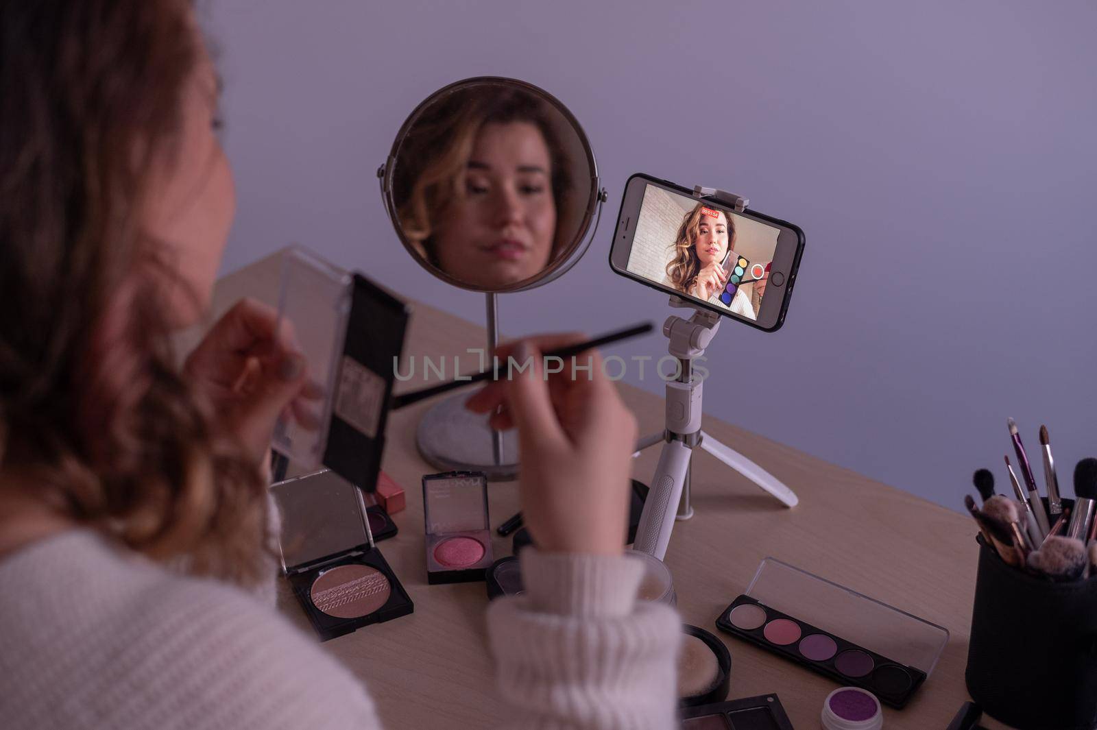 Caucasian woman leads an online make-up lesson for herself on her mobile phone.