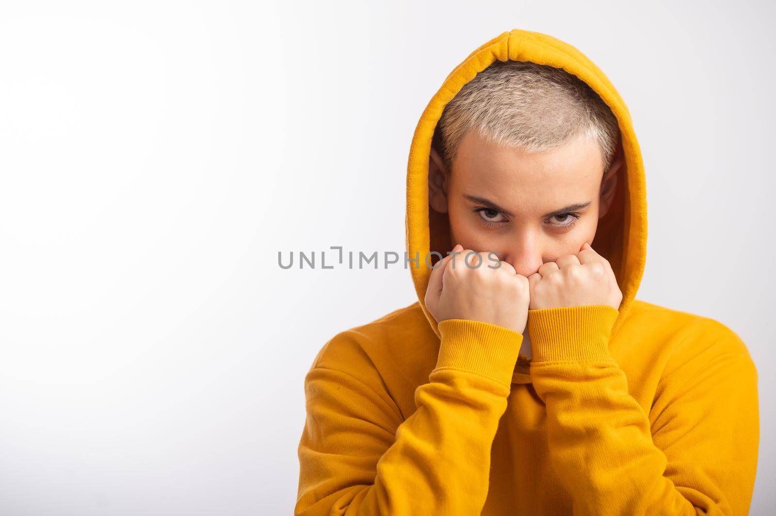 Young woman in ocher hood holding fists near face on white background