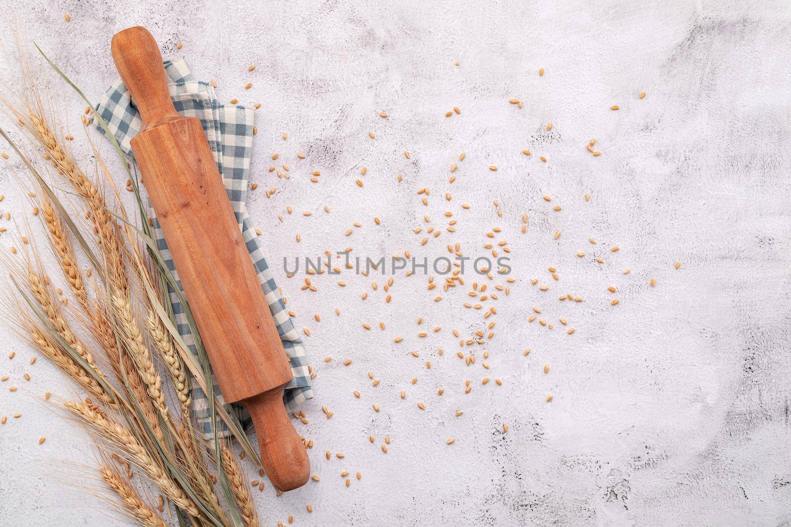 Wheat ears and wheat grains setup with rolling pin on white concrete background. by kerdkanno