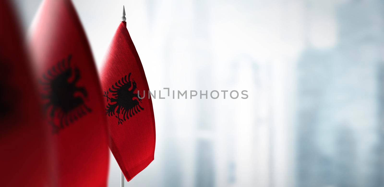 Small flags of Albania on a blurry background of the city.