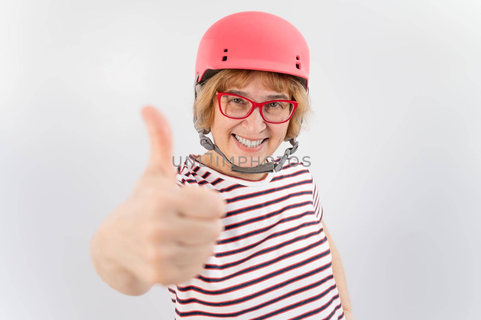 Elderly woman in ski helmet showing thumb up on white background. by mrwed54