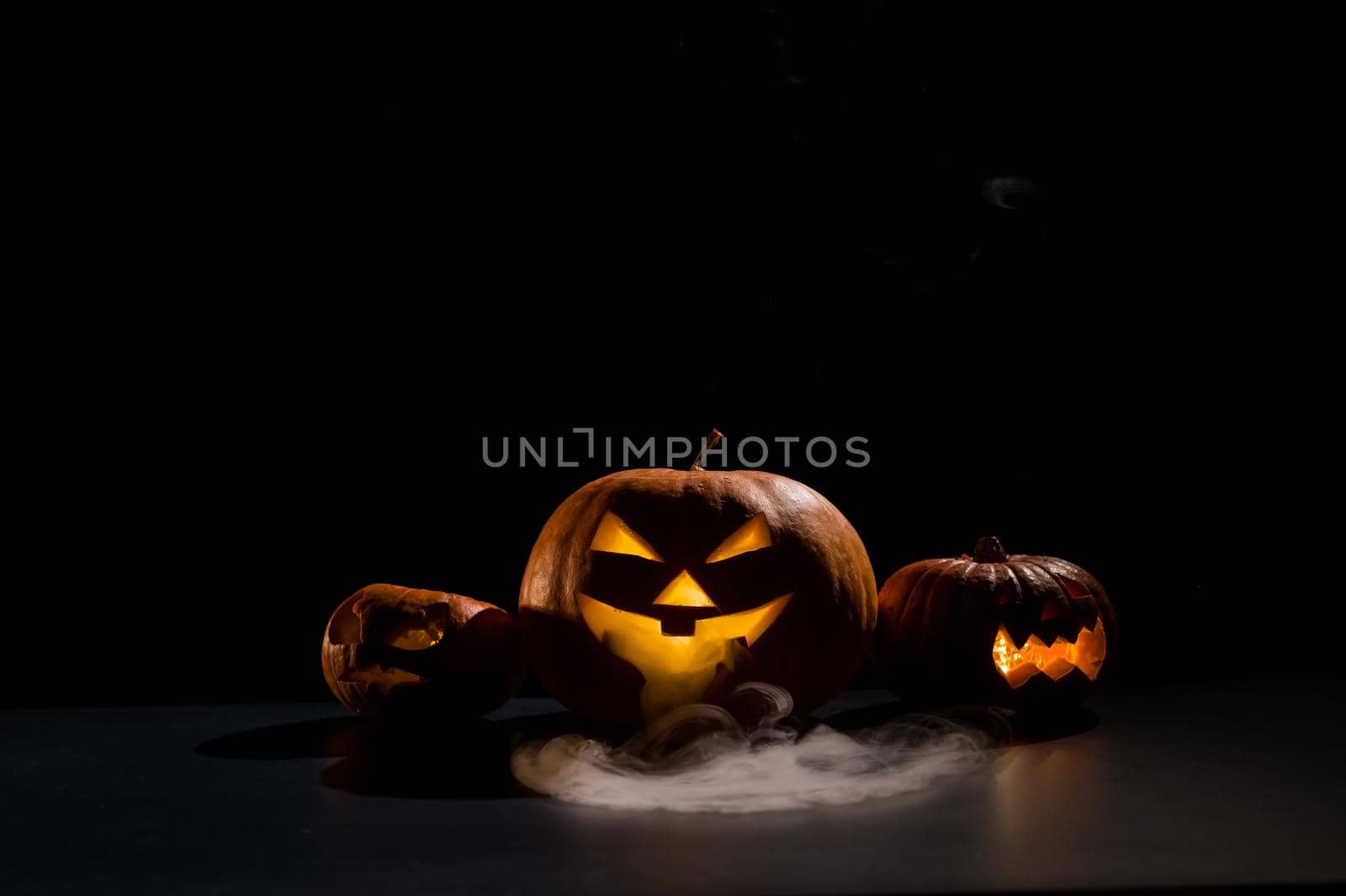Halloween card. jack o lantern with candles glow on a black background. A row of creepy pumpkins with carved grimaces smokes in the dark