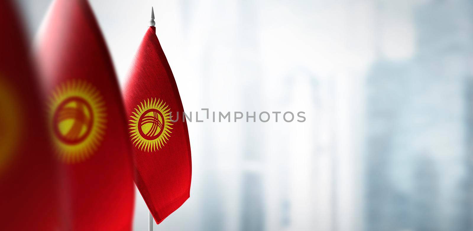 Small flags of Kirghizia on a blurry background of the city by butenkow