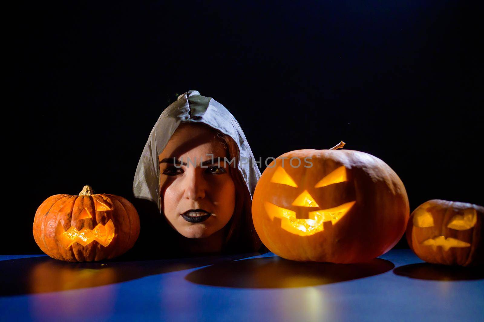 The evil witch casts a spell on pumpkins. Portrait of a woman in a carnival halloween costume in the dark.