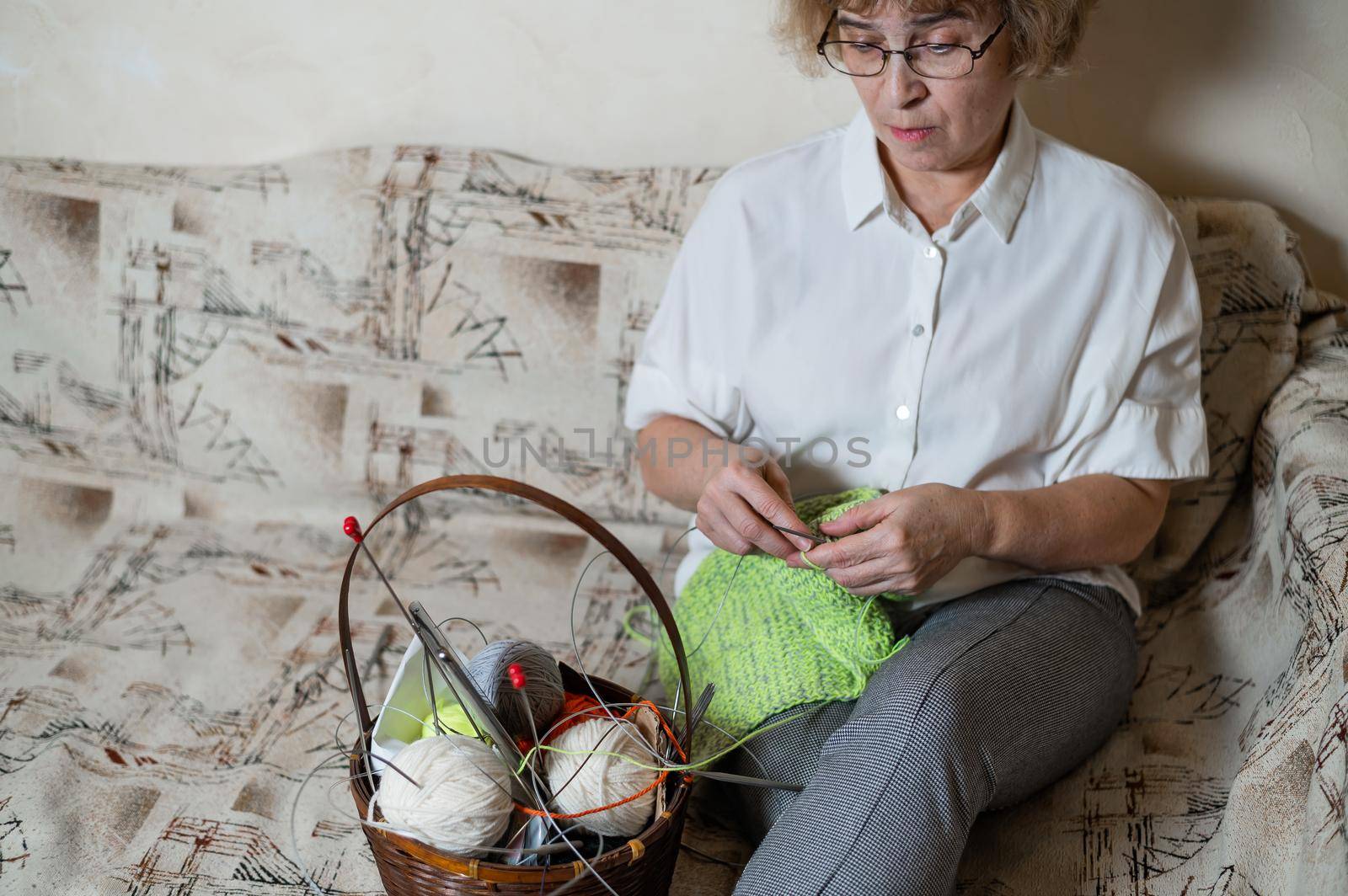 An elderly Caucasian woman knits sitting on a couch