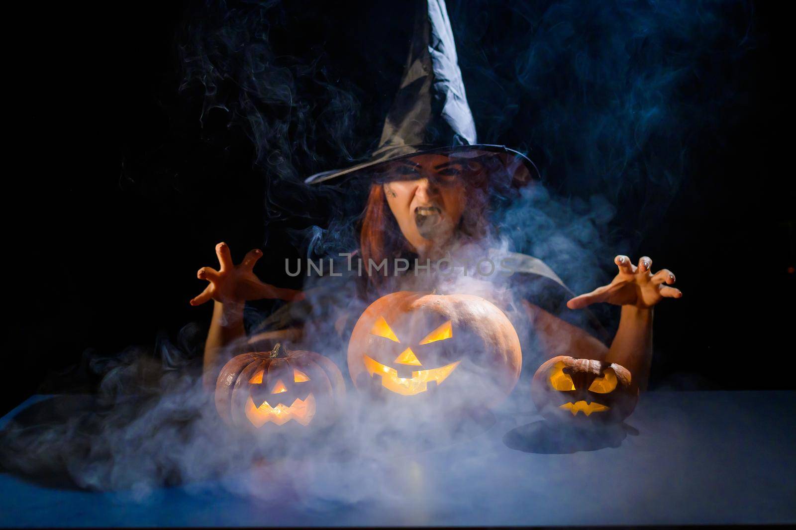 The evil witch casts a spell on pumpkins. Portrait of a woman in a carnival halloween costume in the dark by mrwed54