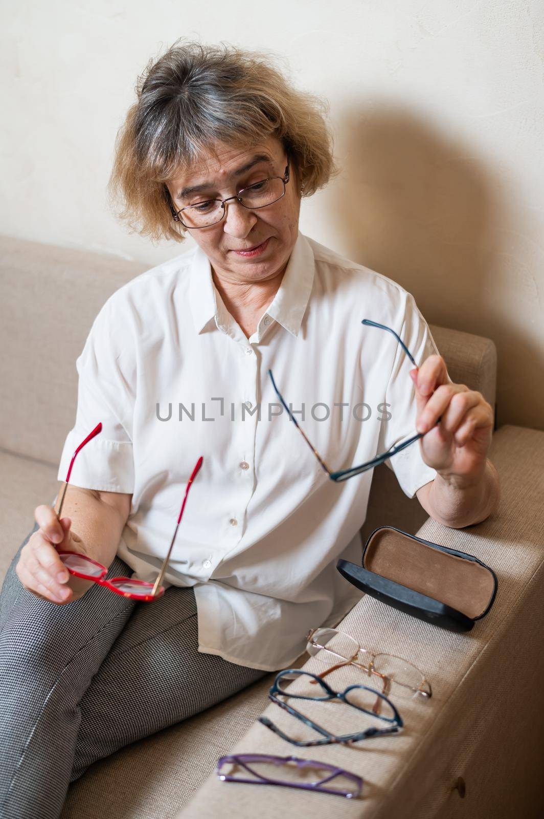 An elderly Caucasian woman chooses glasses from her home collection.