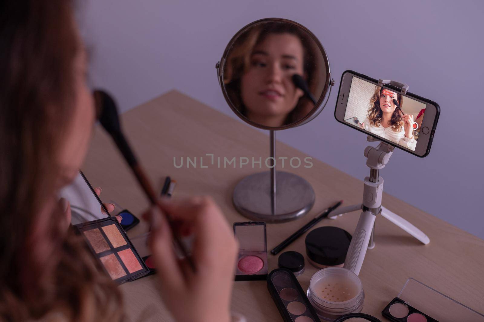 Caucasian woman leads an online make-up lesson for herself on her mobile phone.