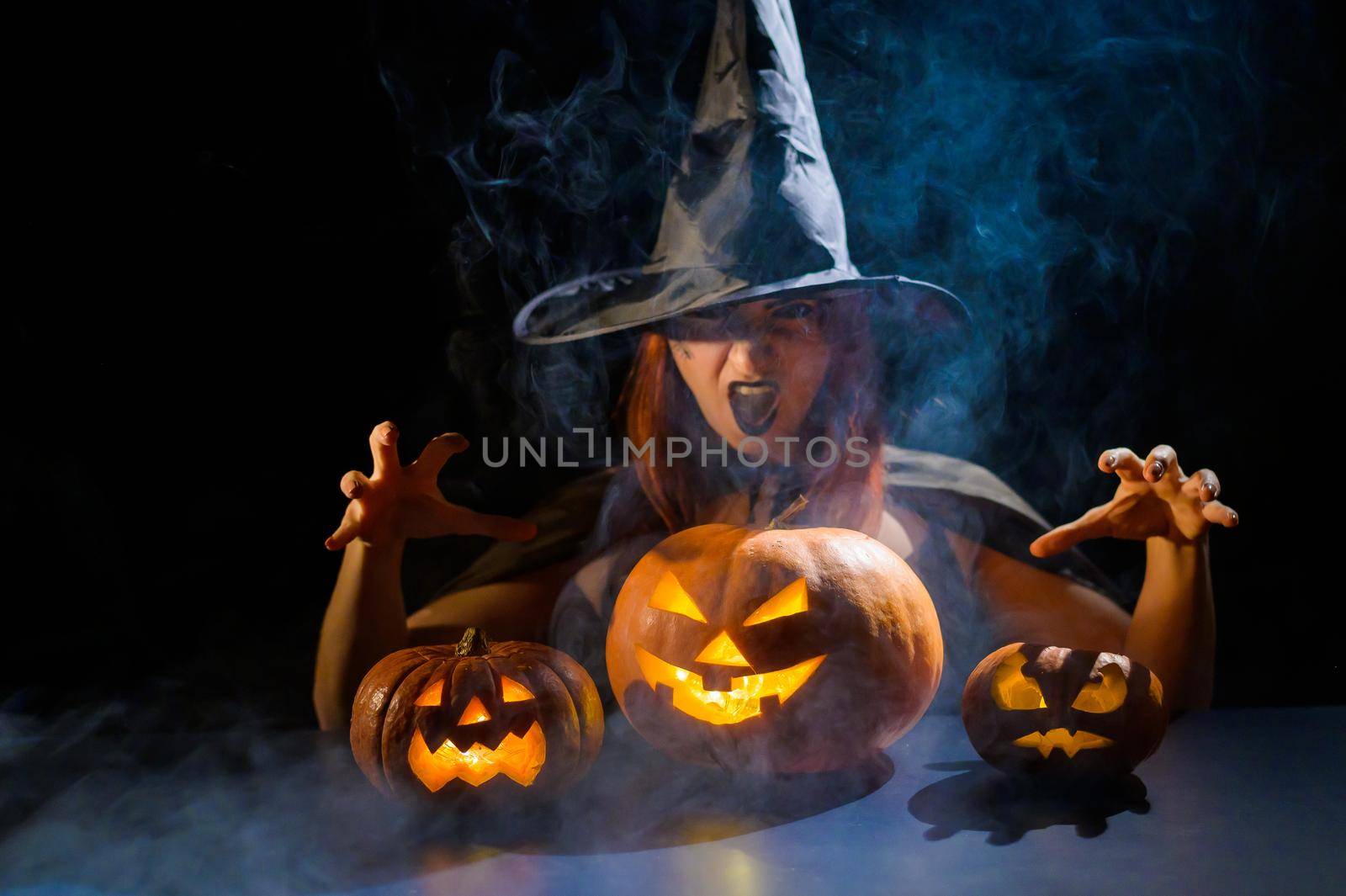 The evil witch casts a spell on pumpkins. Portrait of a woman in a carnival halloween costume in the dark by mrwed54