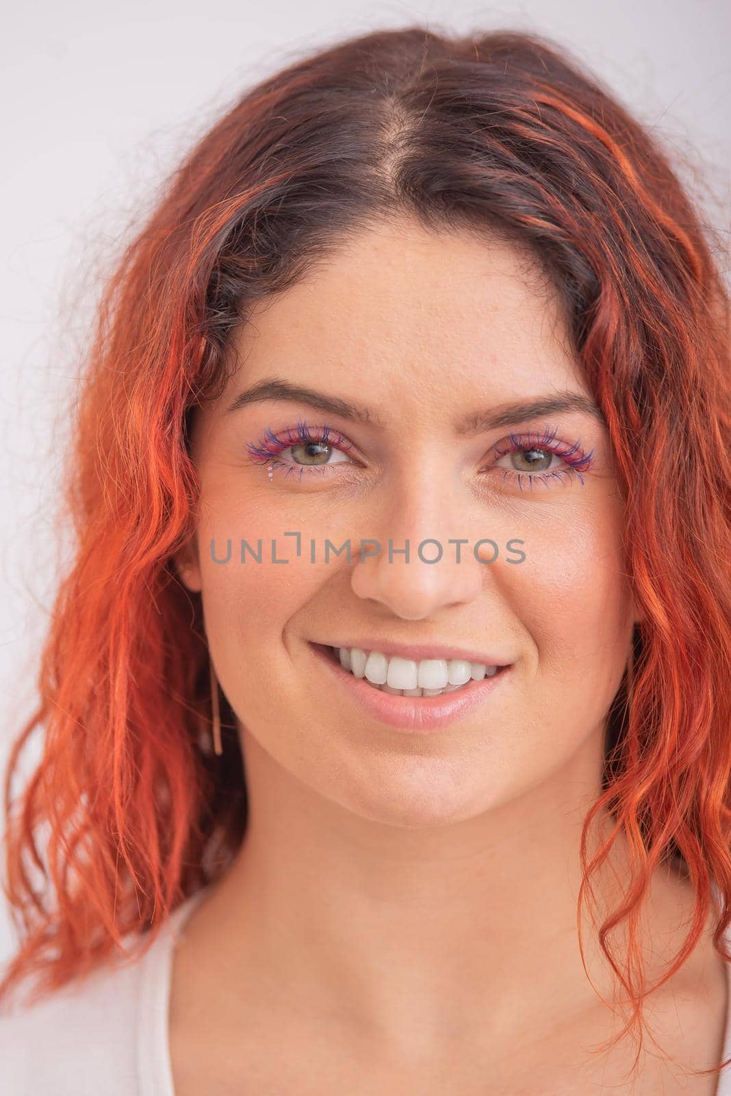Portrait of caucasian red-haired woman with colored eyelashes on white background