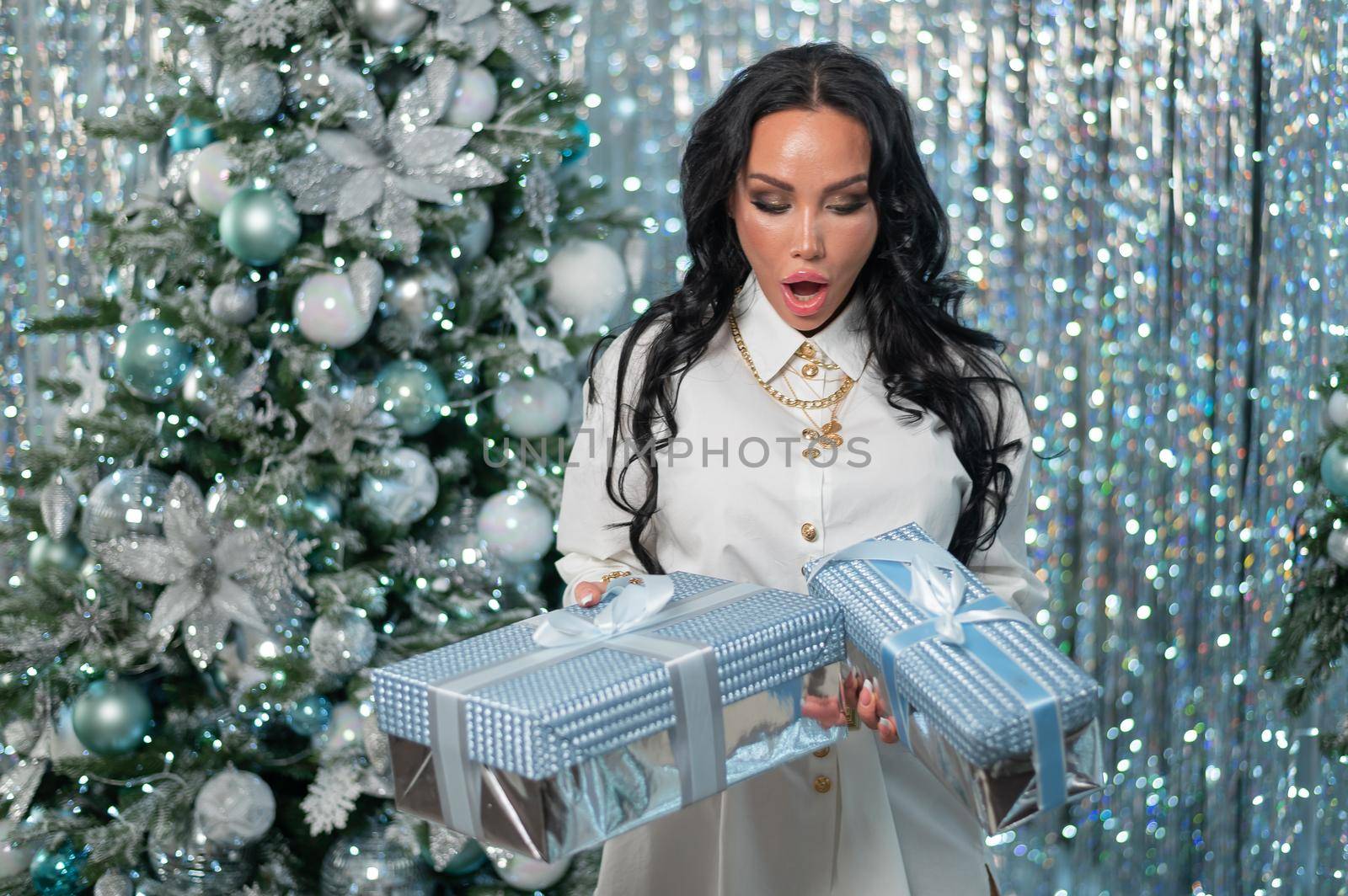 Sexy brunette in a white dress holds gifts by the Christmas tree.